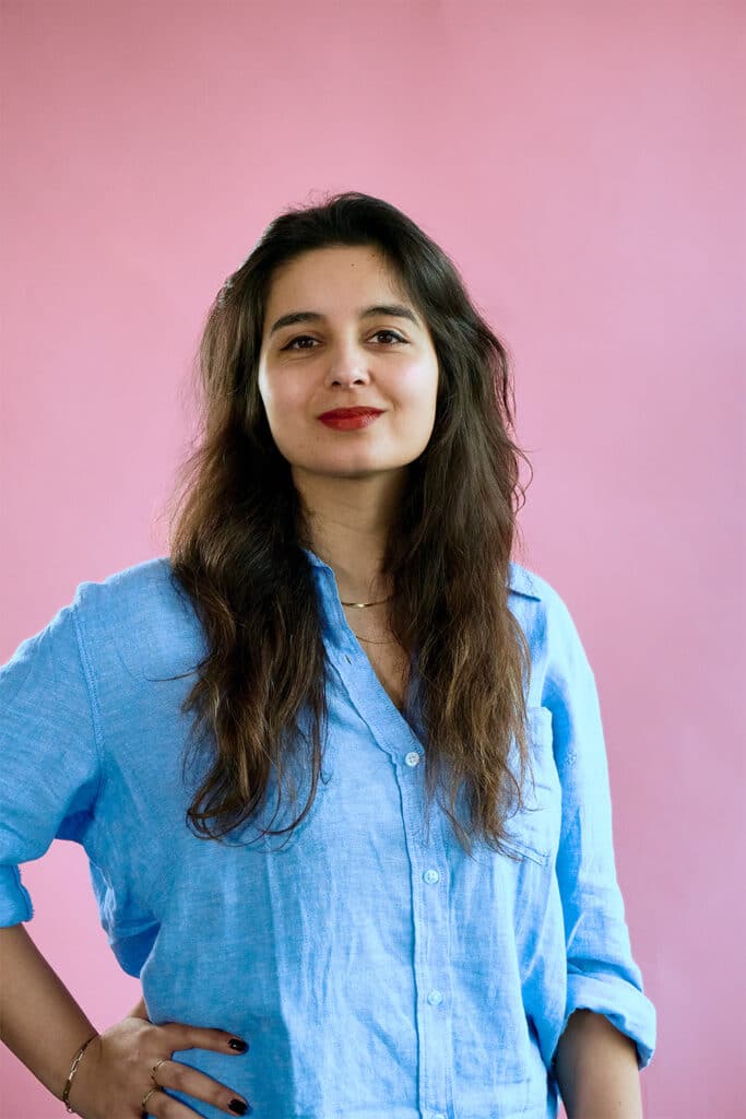 Louisa op een roze achtergrond met een lichtblauwe blouse en de mouwen opgerold