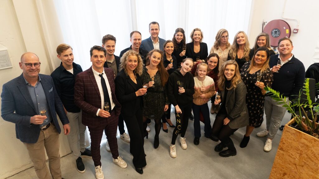 Een lachende groepsfoto van team Clap, ze hebben allemaal een champagne glas in hun hand. Ze kijken allemaal richting de camera.