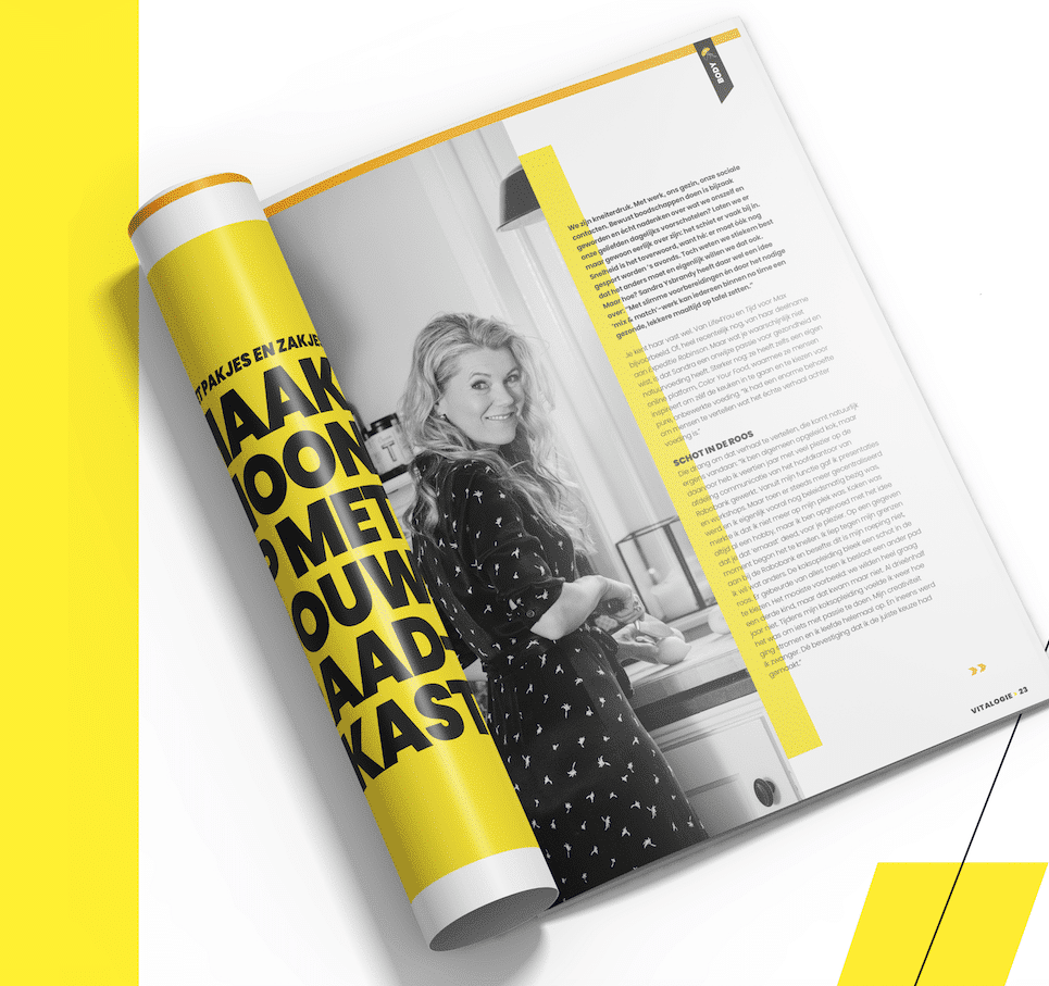 Een opengevouwen magazine met een zwart-wit foto van een vrouw in de keuken. Naast de foto is er een groot geel vlak met tekst en een artikel dat verder gaat op de pagina. De kleuren zijn voornamelijk geel, zwart en wit.