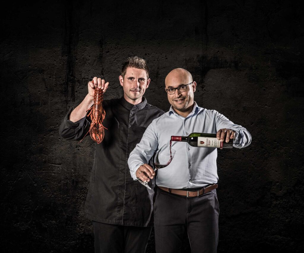 twee mannen met kreeft en fles wijn donkere achtergrond