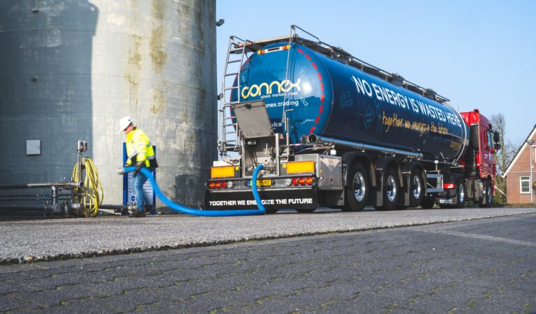 Een hele grote vrachtwagen met 'no energy is wasted here' op de wagen. Achter de wagen staat een man in een fel gele jas met een lange buis in zijn handen.