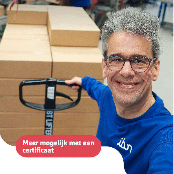 Een man met grijs haar, een bril en een blauwe trui met het logo "ibn" lacht naar de camera terwijl hij een palletwagen vasthoudt. Achter hem staan stapels kartonnen dozen in een magazijnomgeving met andere medewerkers aan het werk. De afbeelding bevat de tekst "Aandacht voor ontwikkeling" en een rode label met de tekst "Meer mogelijk met een certificaat"