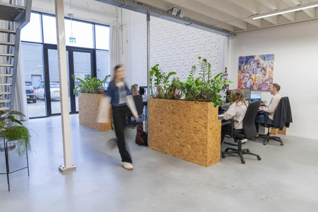 Dame op kantoor die loopt en 2 heren achter een computerscherm op een bureaustoel