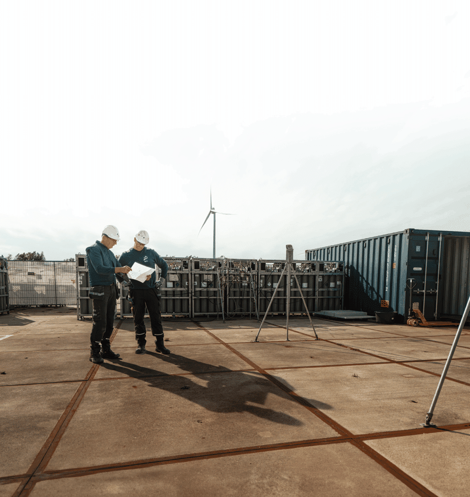 Twee RIFT-medewerkers met veiligheidshelmen bekijken documenten bij een industriële installatie.